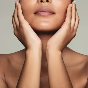 This image features a woman holding a photo of her face with visible sun damage and dark spots, contrasting it with her seemingly clear skin, suggesting a before-and-after of a skin treatment.