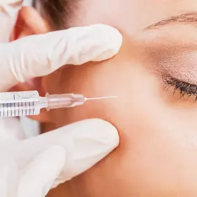 A close-up shows a medical professional in white gloves administering an injection into a person's upper cheek area. The person's eye is closed, and the syringe is clearly visible.