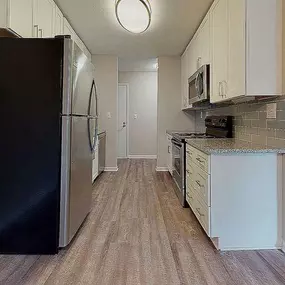 A black refrigerator is in the corner of a kitchen with wood flooring.