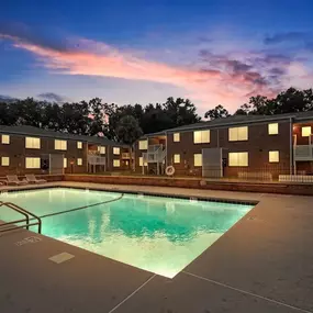 An apartment pool with a sunset in the background at dusk