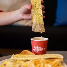 A hand dipping a Cuban toast in Cuban coffee with milk.