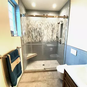 A professional is mulching an overgrown wooded area with a yellow Vermeer S925TX mini skid steer. Trees stand in the background, and the ground is covered in wood chips.