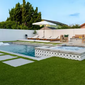 Custom-designed backyard with swimming pool, with built-in spa, lounge area, fire pit, and artificial grass surface with concrete tiles.