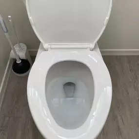 This overhead shot showcases a sparkling clean white toilet with its lid open, revealing a spotless bowl. A toilet brush and plunger are neatly positioned beside it. The entire area appears meticulously cleaned, highlighting a high standard of bathroom hygiene.