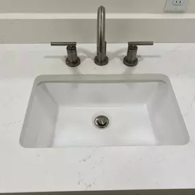 This close-up shows a pristine white bathroom sink with sleek, modern brushed nickel fixtures set into a light-colored, subtly veined countertop. The surfaces are spotless, indicating a thorough cleaning, ready for immediate use.