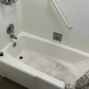 This image shows a white bathtub with a visibly dirty, scuffed surface and sediment at the bottom, indicating a need for deep cleaning. The surrounding white walls have a grab bar and soap dish, suggesting a bathroom awaiting a thorough cleaning.