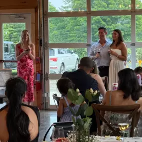 A heartfelt toast at a private rehearsal dinner held at Tranquillity Vineyard & Winery in Middlebury, CT. A guest in a floral dress speaks warmly while a smiling couple stands with wine glasses in hand, surrounded by friends and family.