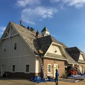 An exterior shot of a house under construction shows the wooden roof trusses and plywood sheathing. In the background, other houses and a road are visible.