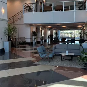 Step into our modern, open-concept lobby featuring sleek marble floors, high vaulted ceilings, and abundant natural light. Comfortable seating, curated artwork, and lush greenery create a calm, professional atmosphere from the moment you arrive. Located just beyond the elegant staircase and main atrium, our clinic offers a serene setting designed to support your wellness journey in both comfort and style.