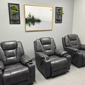 This IV therapy room offers a calm, comfortable, and spa-like environment designed to support relaxation during treatment. It features three plush, charcoal leather recliners—each equipped with cup holders and remote controls for personalized positioning. The space is accented with minimalist decor, including two bonsai-themed wall frames and a tranquil landscape painting, creating a peaceful ambiance. Soft gray walls and flooring further enhance the clean, modern aesthetic.

Ideal for extended 