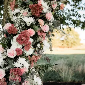 A tree in a meadow decorated in a custom handmade floral arrangement of pink, red, and white shades, for bride and groom pictures, designed by Christina Price, wedding floral designer in Hagerstown.