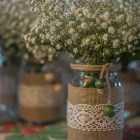 Mason jars decorated with flowers in them as table arrangements customized by Christina of Homestead Floral Wedding & Events.