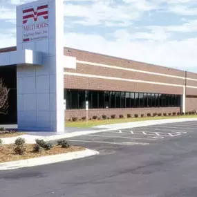 Exterior of the Methods Machine Tools facility in Charlotte, North Carolina with a long brick façade, modern entry column, and a spacious, well-maintained parking area.