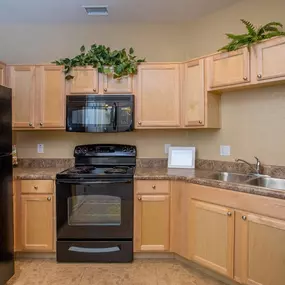 A kitchen with wooden cabinets with a black refrigerator and black appliances.