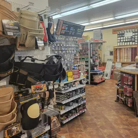 A Builders FirstSource store interior showing a display of tool belts, knee pads, and various building supplies organized on shelves. The setup includes racks with small construction essentials like screws, nails, and fasteners, alongside other tools and accessories. In the background, signs highlight sections of the store, creating a welcoming and well-organized shopping area for customers.