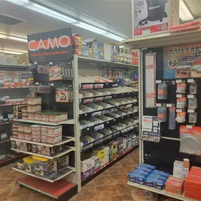 An interior aisle at Builders FirstSource, showcasing a variety of deck-building and railing products. The display includes a prominent CAMO section, with boxes of screws, fasteners, and tools labeled 