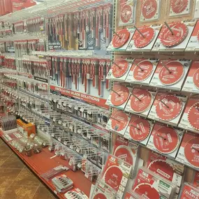 A well-stocked aisle in a Builders FirstSource store featuring a display of Diablo circular saw blades and Milwaukee oscillating tool blades. The display includes various blade sizes and types, organized neatly on peg hooks for easy browsing. Each product is arranged with its packaging facing outward, clearly labeled, showcasing a comprehensive selection of cutting solutions for wood, metal, and other materials. The tiled flooring and organized shelving enhance the store's professional and invit