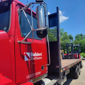 Builders FirstSource flatbed delivery truck with red cab and piggyback Moffett.