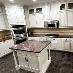 Finished kitchen remodel featuring white cabinets and a contrasting dark island with bar seating and modern lighting.
