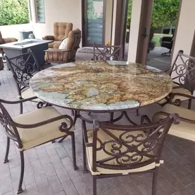 An outdoor patio with a large round table featuring a mottled granite top and several ornate metal chairs.