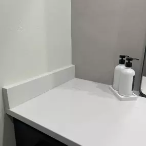 A clean, modern bathroom countertop with a white quartz surface, backsplash, and two soap dispensers.