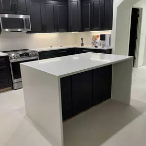 A spacious, modern kitchen featuring dark cabinets, light countertops, and a large white island with a waterfall edge.