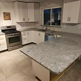 A kitchen under renovation with white cabinets, speckled gray granite countertops, and stainless steel appliances.