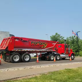 Red Forbes Asphalt dump truck parked on roadside, surrounded by traffic cones.