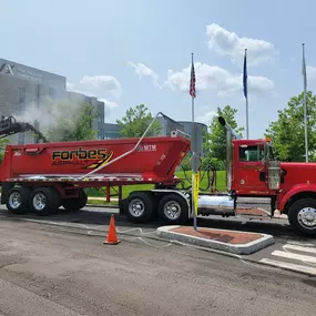 Forbes Asphalt truck positioned under milling equipment during active road surface removal.