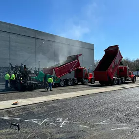 A team from Forbes Asphalt paving a commercial lot using dump trucks and a paver.