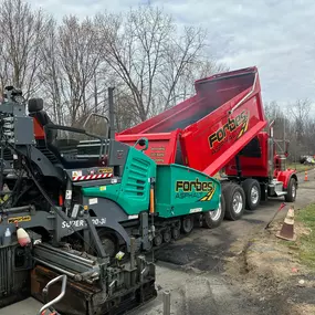 Close-up of the paving process with a Forbes Asphalt dump truck feeding asphalt into a paver.
