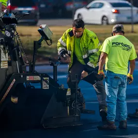 Workers preparing asphalt during a paving job, highlighting manual detail work.