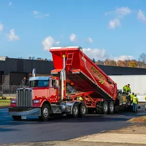 Red Forbes Asphalt dump truck unloading hot asphalt during a large-scale paving project.