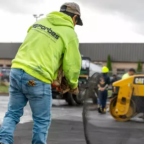 A worker spreading asphalt by hand while wearing a branded safety hoodie