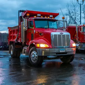Front view of a Peterbilt dump truck branded with the Forbes Asphalt logo, headlights on at dusk.