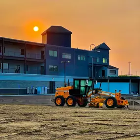 Grading equipment parked at a construction site during a vivid orange sunset.