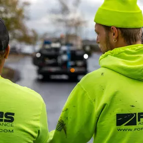Two Forbes Asphalt team members in safety hoodies observing equipment down the worksite path.