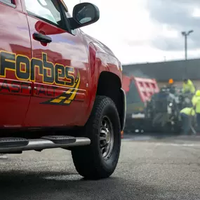 Close-up of a red Forbes Asphalt truck with worksite activity in the background.