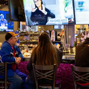 A couple relaxes at the bar enjoying their drinks while large flat-screen TVs play sports and entertainment—capturing Brewbury’s casual viewing experience