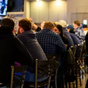 A rear view of guests gathered at the bar, enjoying food, drinks, and conversation while surrounded by TVs and warm lighting