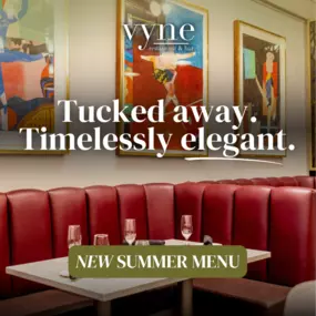 The interior of Vyne Restaurant & Bar, where elegance meets artistry. Cozy red banquette seating beneath vibrant framed art.