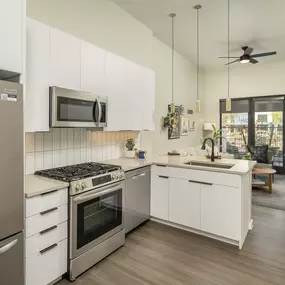 A modern kitchen with gas stove, stainless steel appliances, quartz counters and white cabinetry.