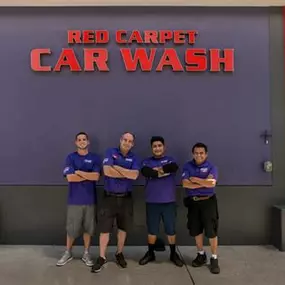 Four smiling team members stand under the Red Carpet Car Wash logo at the Manhattan Beach location. Reflects professionalism, friendly customer service, and a unified brand identity.