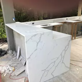 An outdoor kitchen under construction, featuring newly installed white quartz countertops and a waterfall island with elegant grey veining, demonstrating quality stone fabrication and installation.
