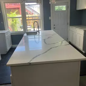 A newly installed kitchen island features a gleaming white quartz countertop with prominent grey veining, complementing the white cabinetry and pale blue walls, showcasing elegant stone work.