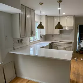 A kitchen under renovation features newly installed sleek white countertops, contrasting with light-colored cabinets and bare walls awaiting a backsplash, showcasing the fresh stone installation.