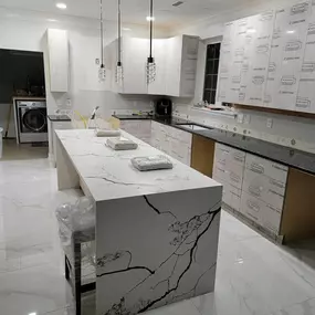 A spacious, modern kitchen undergoing finishing touches, featuring a large island with a stunning white countertop and bold black veining, complemented by dark perimeter counters and light cabinetry.