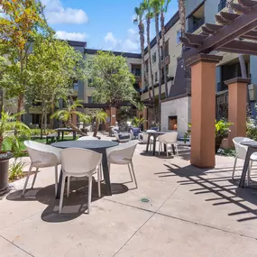 A patio with tables and chairs is surrounded by plants and trees.