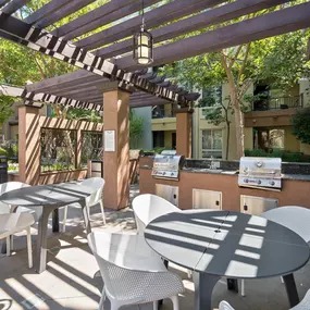A patio with white chairs and tables is covered by a striped awning.