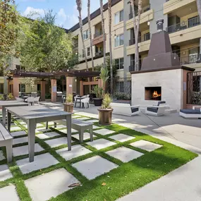 A patio with a table and chairs is surrounded by a grassy area and apartment buildings.